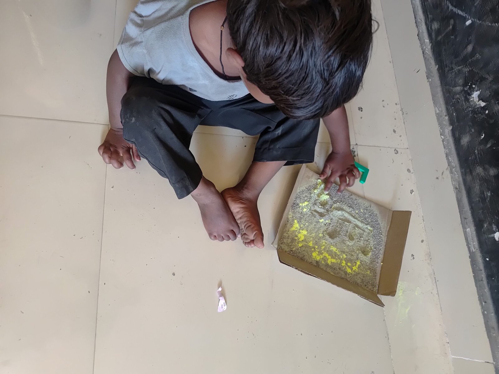 आंगनबाड़ी केंद्र में बच्चा रेत लेखन गतिविधि करते हुए